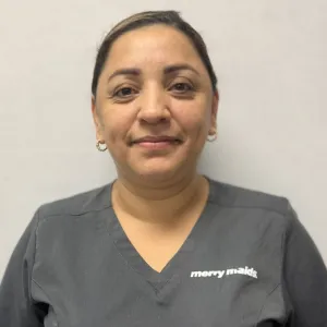 smiling woman with a grey merry maids uniform standing in front of a tan wall
